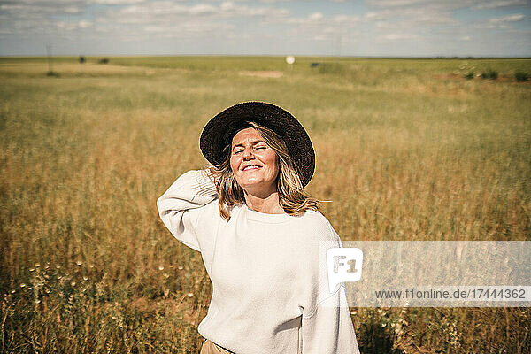 Smiling woman with eyes closed wearing hat at field