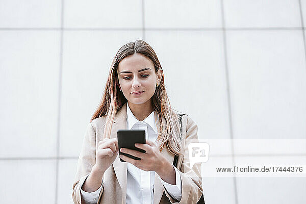 Female business professional using smart phone in front of wall
