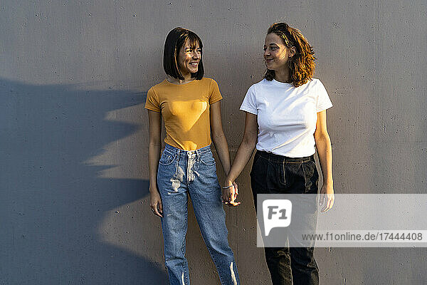 Lesbian couple holding hands while standing in front of wall