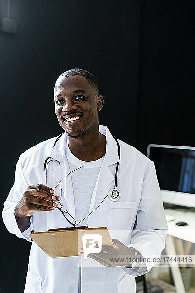 Happy healthcare worker with eyeglasses and clipboard at medical clinic