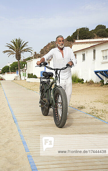 Mature man wheeling bicycle on boardwalk