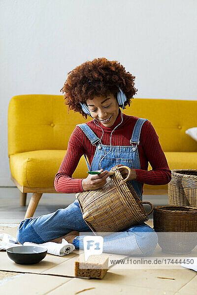 Woman wearing headphones painting wicker basket in living room
