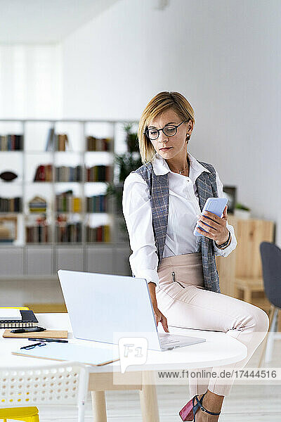 Eine berufstätige Frau im mittleren Erwachsenenalter benutzt einen Laptop  während sie im Büro am Schreibtisch sitzt