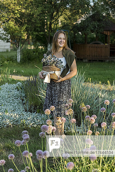 Smiling woman walking while holding basket of globe thistle in back yard