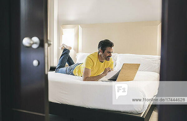 Smiling businessman working on laptop in bedroom