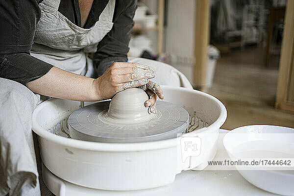 Female potter molding clay on pottery wheel in workshop