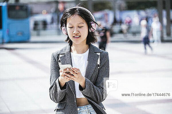 Teenagermädchen trägt an einem sonnigen Tag kabellose Kopfhörer und nutzt ihr Mobiltelefon