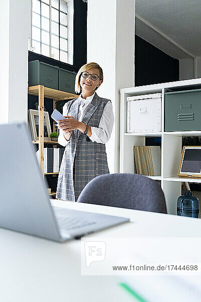 Smiling mid adult businesswoman holding mobile phone in office