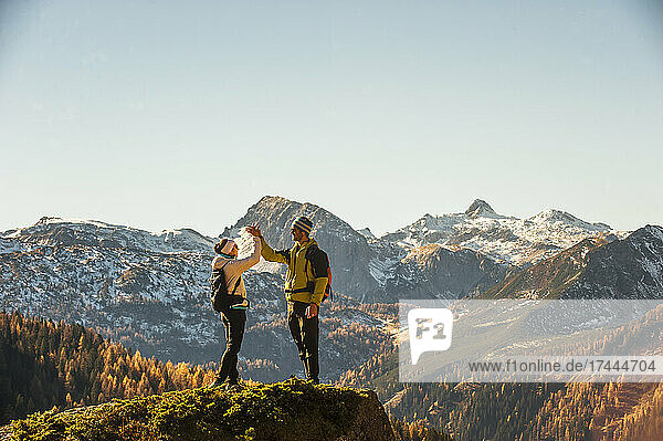 Two hikers high-fiving on top of edge in Ennstal Alps