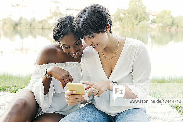 Happy lesbian couple sharing mobile phone at lakeshore