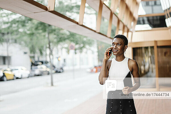 Smiling businesswoman holding digital tablet while talking on smart phone