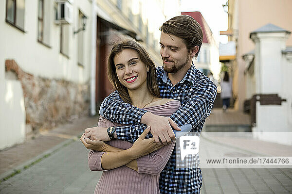 Smiling boyfriend standing with arm around girlfriend on footpath