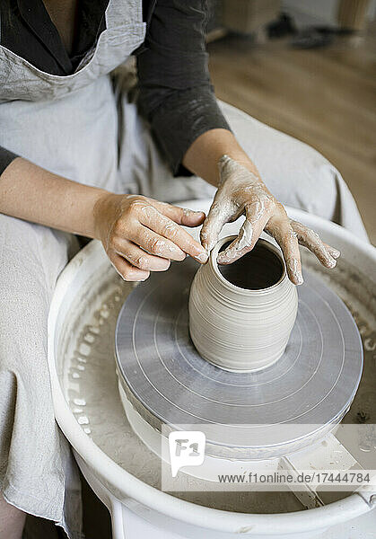 Female potter molding shape on pottery wheel in workshop