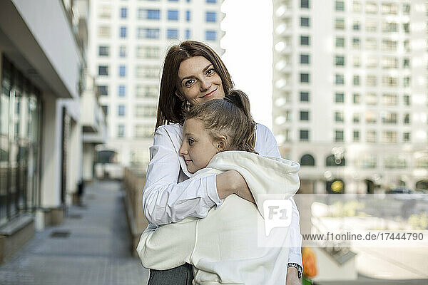 Smiling mother embracing daughter in city