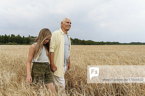 Girl holding hand of grandfather while walking on wheat field