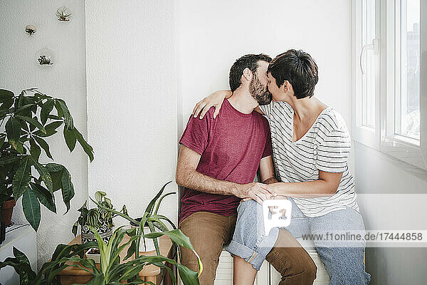 Man and woman kissing while sitting near plants at home