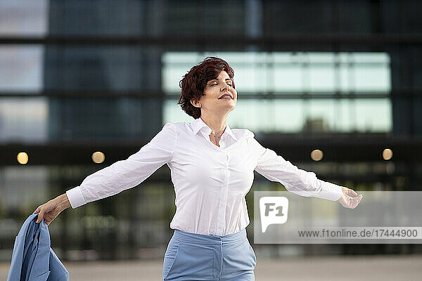 Schöne Geschäftsfrau mit ausgestreckten Armen tanzt vor dem Bürogebäude