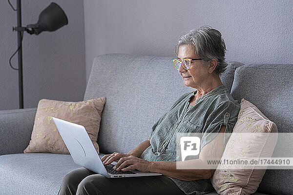 Ältere Frau benutzt Laptop  während sie zu Hause auf dem Sofa sitzt