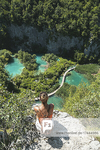 Female hiker admiring landscape of Plitvice Lakes National Park from edge of cliff