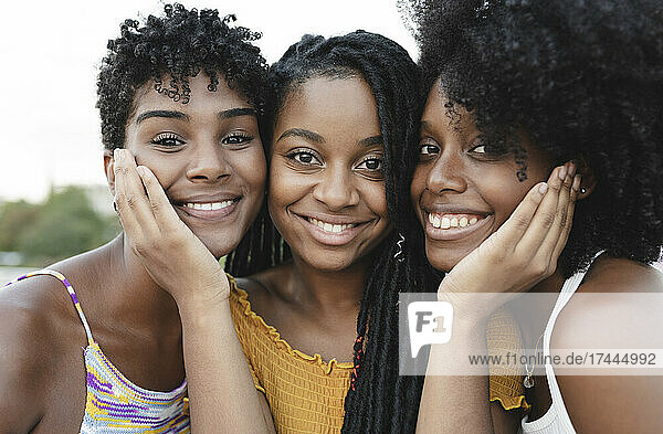 Smiling young woman touching cheeks of female friends
