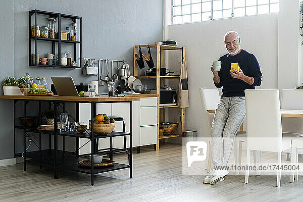 Man having coffee while using mobile phone at home