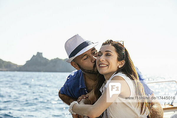 Mann küsst Frau  während er sich an die Reling eines Motorboots lehnt