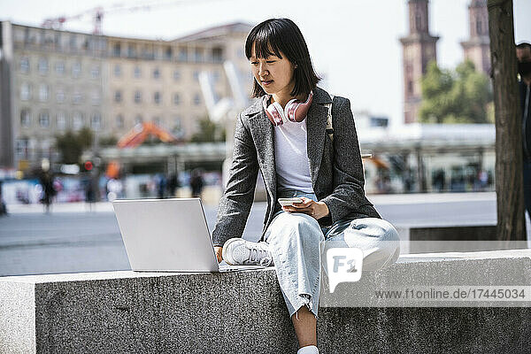 Businesswoman using laptop while sitting on retaining wall