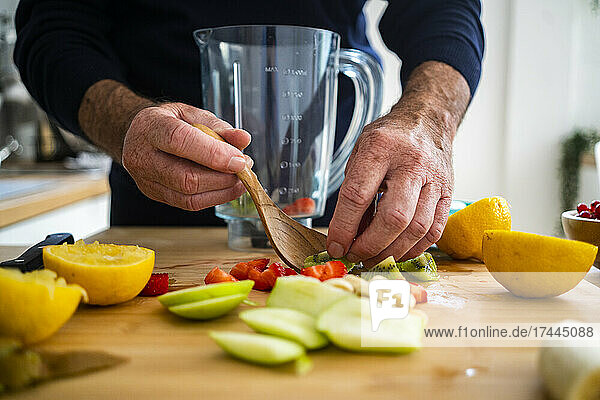 Man making smoothie with fruits at kitchen counter
