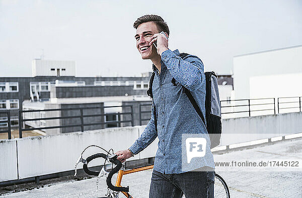 Happy young man with bicycle talking on smart phone