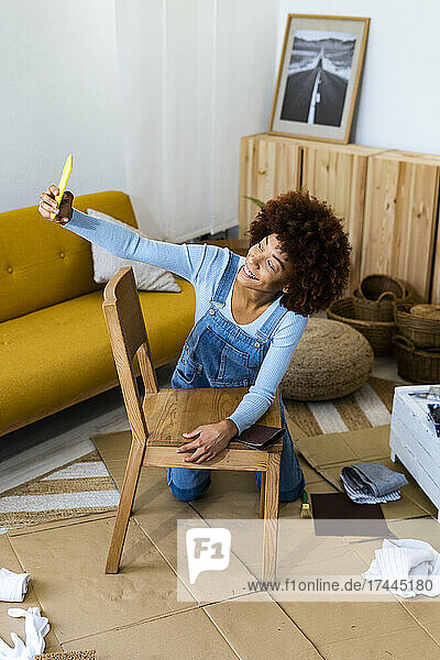Frau mit Holzstuhl macht Selfie mit Smartphone im Wohnzimmer