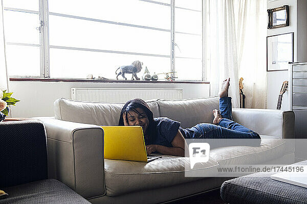 Frau mittleren Alters benutzt Laptop auf Sofa im Wohnzimmer