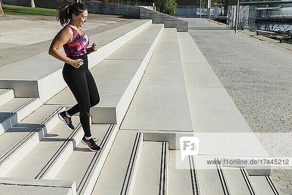 Sportswoman moving down on steps while exercising during sunny day