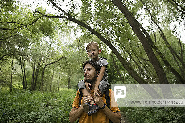 Father carrying son on shoulders while hiking in forest