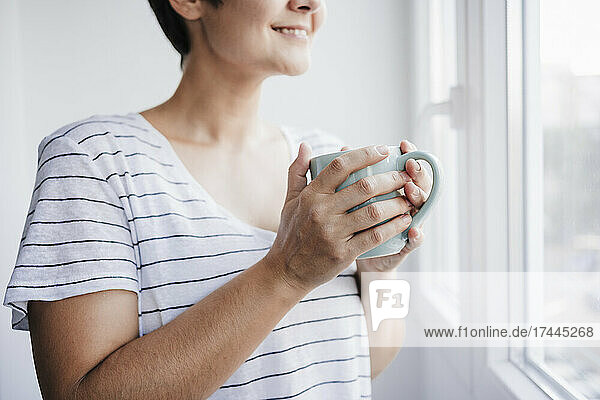 Woman holding mug near window at home