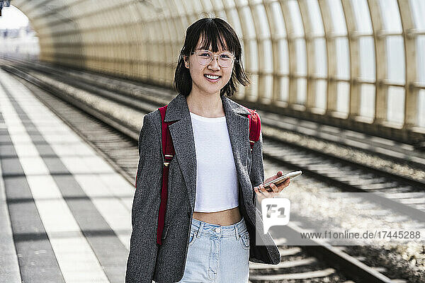 Female teenager with mobile phone and backpack at train station