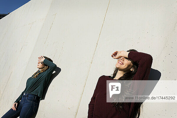 Female friends shielding eyes while leaning on wall