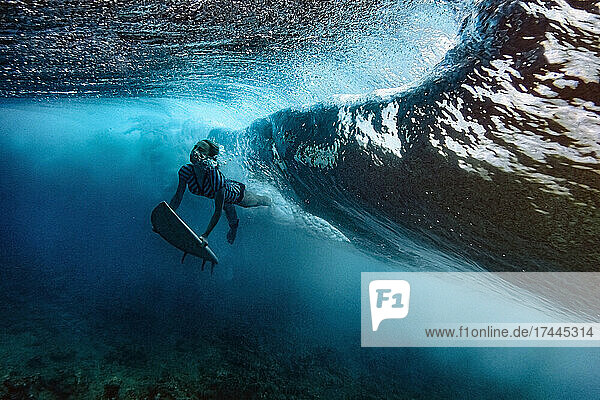 Woman with surfboard diving under waves