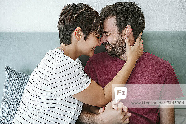 Woman rubbing nose with man while sitting on bed