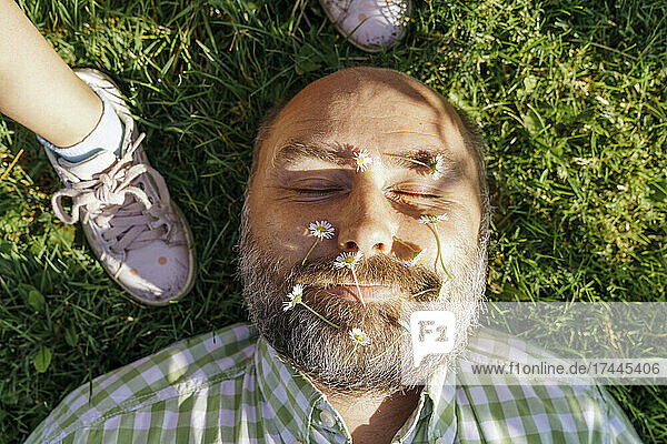 Man with flowers on face lying on grass by daughter
