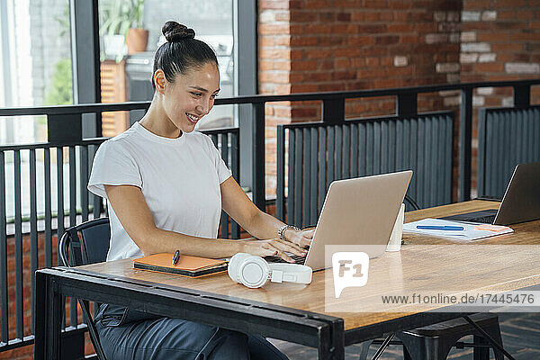 Smiling female professional using laptop while sitting t desk in office