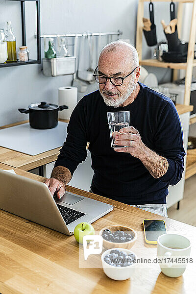 Senior man drinking water while using laptop at home