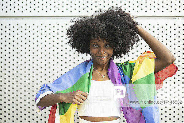 Afro woman wearing pride flag standing in front of metal wall