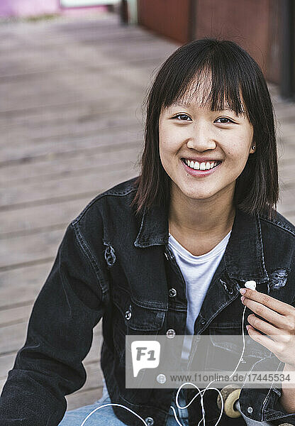 Smiling female teenager sitting on boardwalk