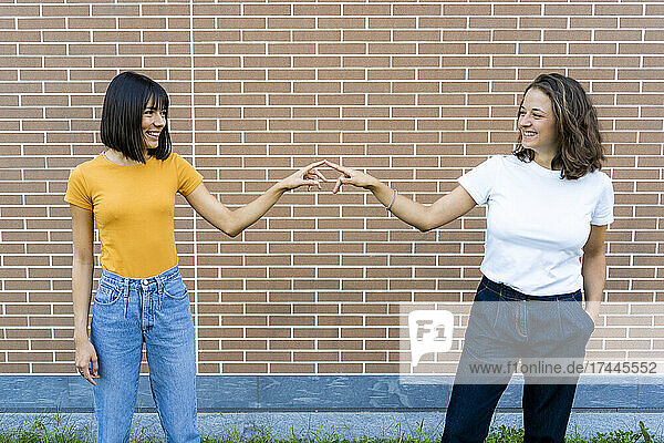 Happy couple pointing at each other in front of brick wall
