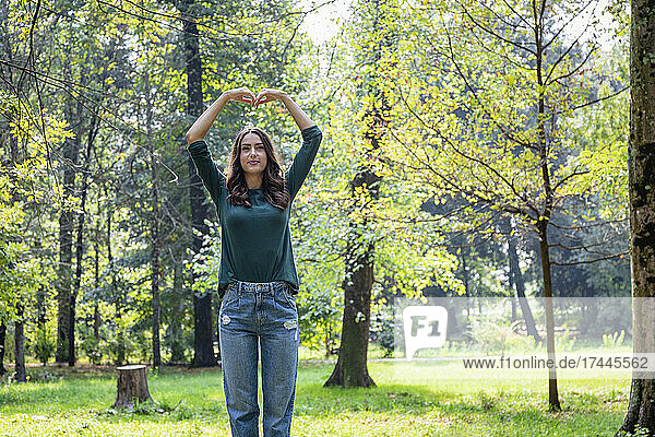Young woman making heart shape with hands at park