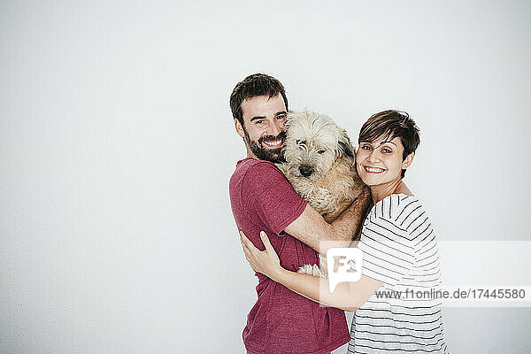 Happy mid adult couple holding pet dog in front of wall