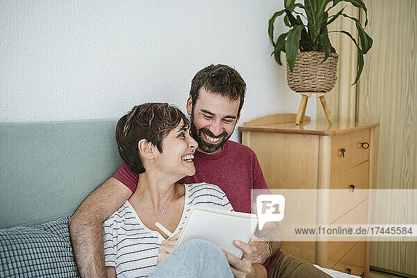 Glückliches Paar mit Notizbuch  das zu Hause im Bett sitzt