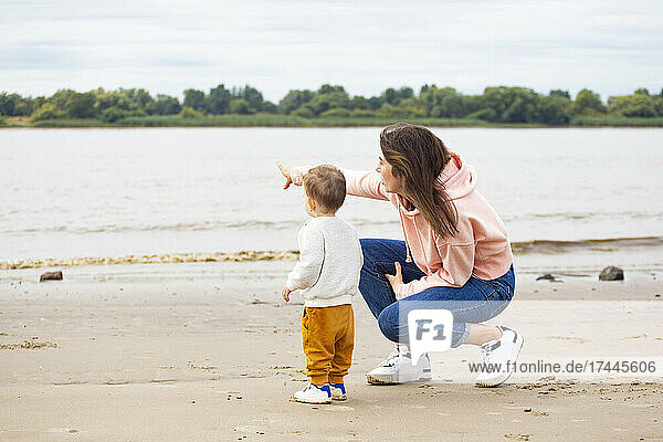 Mutter zeigt  während sie neben ihrem Sohn am Strand hockt
