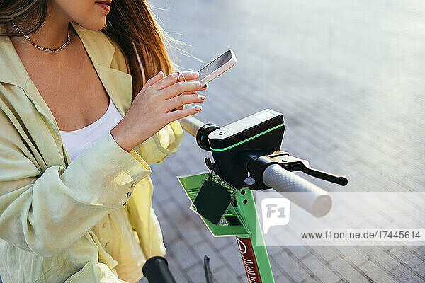 Woman unlocking electric push scooter through mobile phone on road