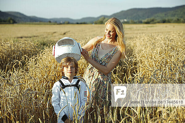 Happy mother holding space helmet while standing with son at field